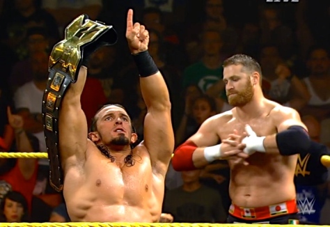 A very confident (almost cocky) Adrian Neville poses with the NXT Championship as Sami Zayn waits.